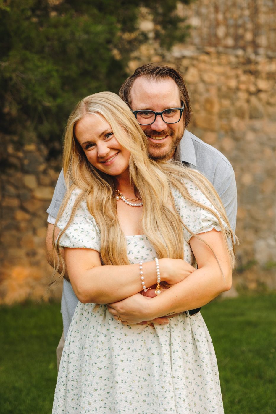 Collin and Becca smiling in front of a stone wall
