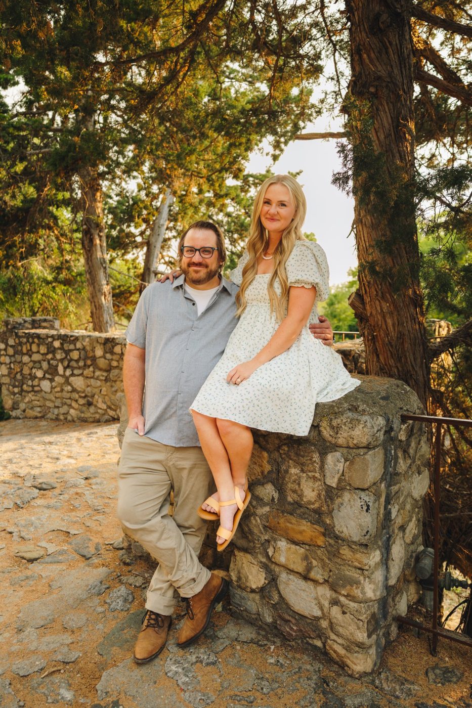 Collin and Becca by a stone wall under juniper trees